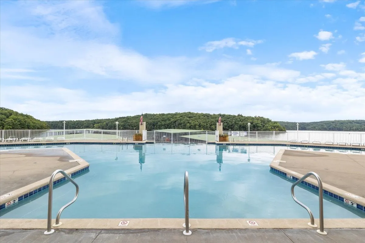 This image features an inviting outdoor swimming pool surrounded by railings and lush landscape, with distant hills providing a scenic backdrop. The tranquil setting suggests opportunities for both sunbathing and relaxing swims, evoking a resort-like atmosphere ideal for summer relaxation.
