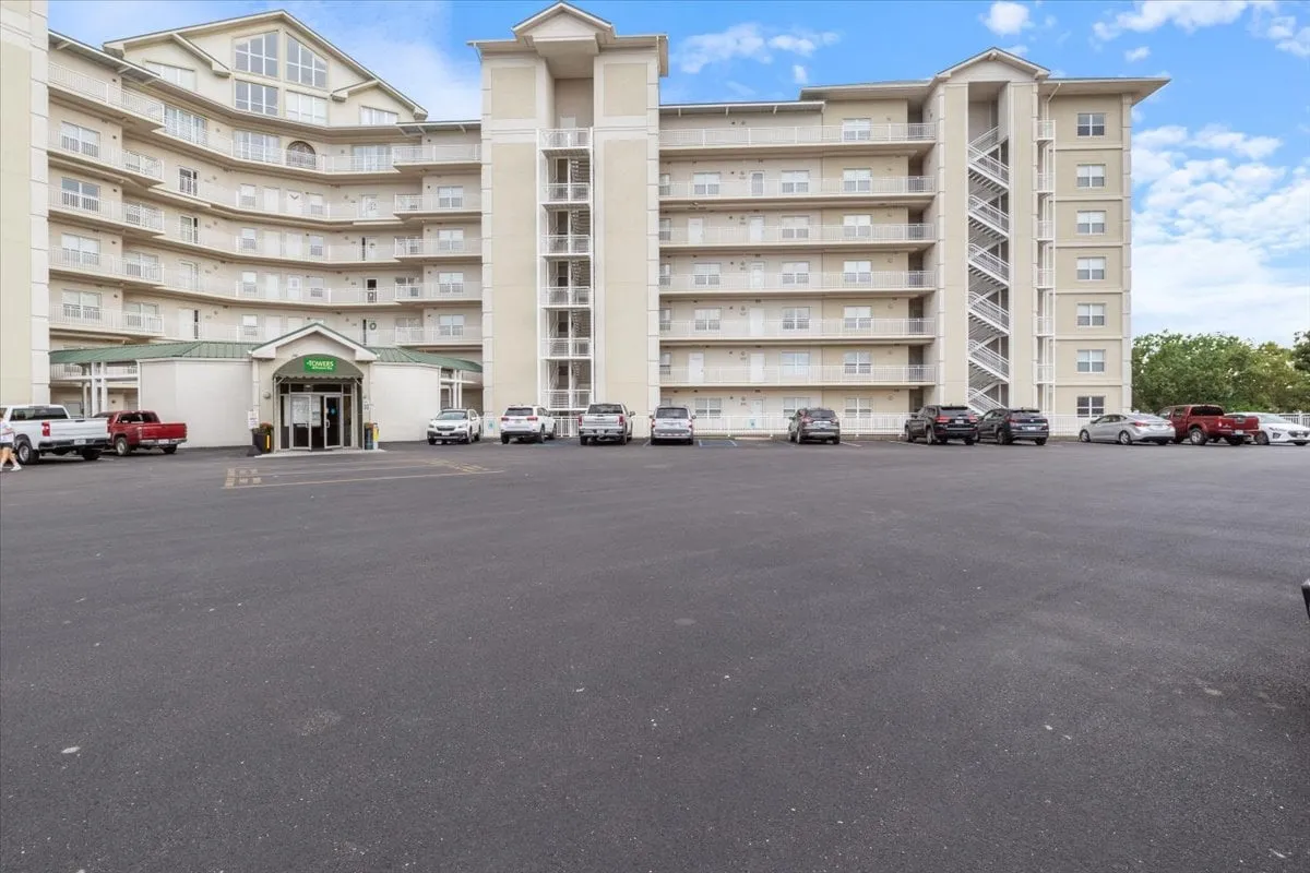 This exterior image captures the main entrance of the property, featuring visible balconies and a welcoming parking lot. The scene suggests both arrival and social gathering opportunities, with hints of communal activities and easy access to nearby attractions.