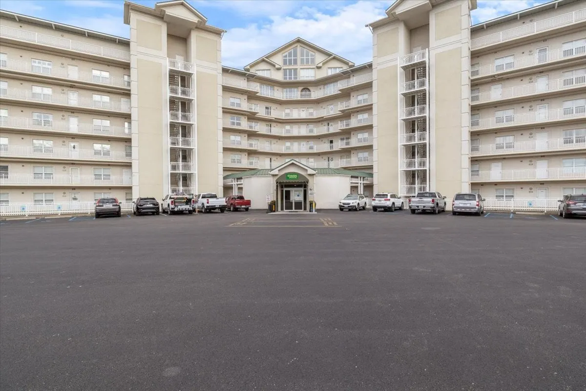 A wide exterior shot of the main entrance, complete with balconies and a spacious parking area. The welcoming atmosphere suggests ease of arrival and ample space for family gatherings, perfect for groups coming together and setting out to local attractions.