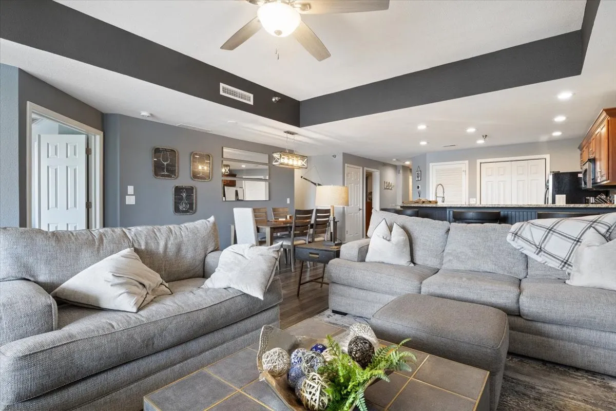 A wide-angle view of the main gathering area, showing sofas, a coffee table, the dining area, and the kitchen in one cohesive, open space. The arrangement is inviting and encourages group activities like games or shared meals.