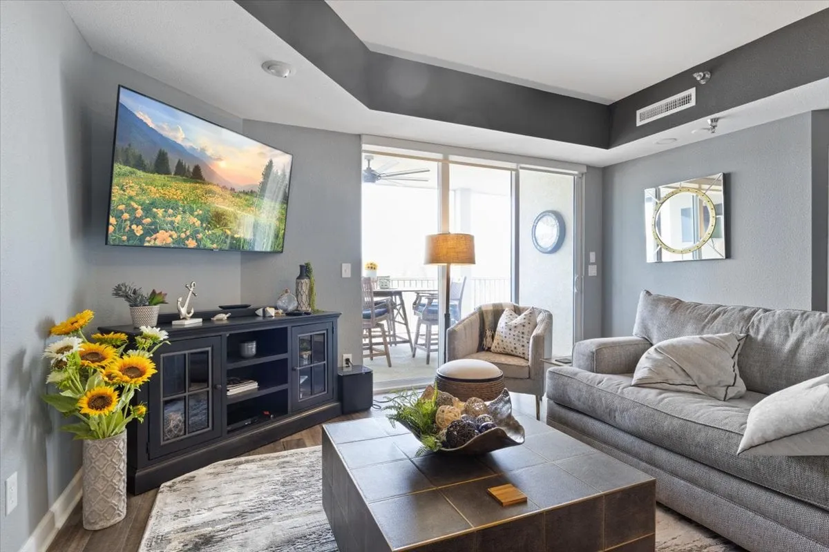 A cozy living area with a large TV displaying a scenic landscape, a welcoming coffee table centerpiece, and fresh sunflowers in a vase. The space invites group relaxation, pre-nightlife gatherings, or unwinding after an evening out.