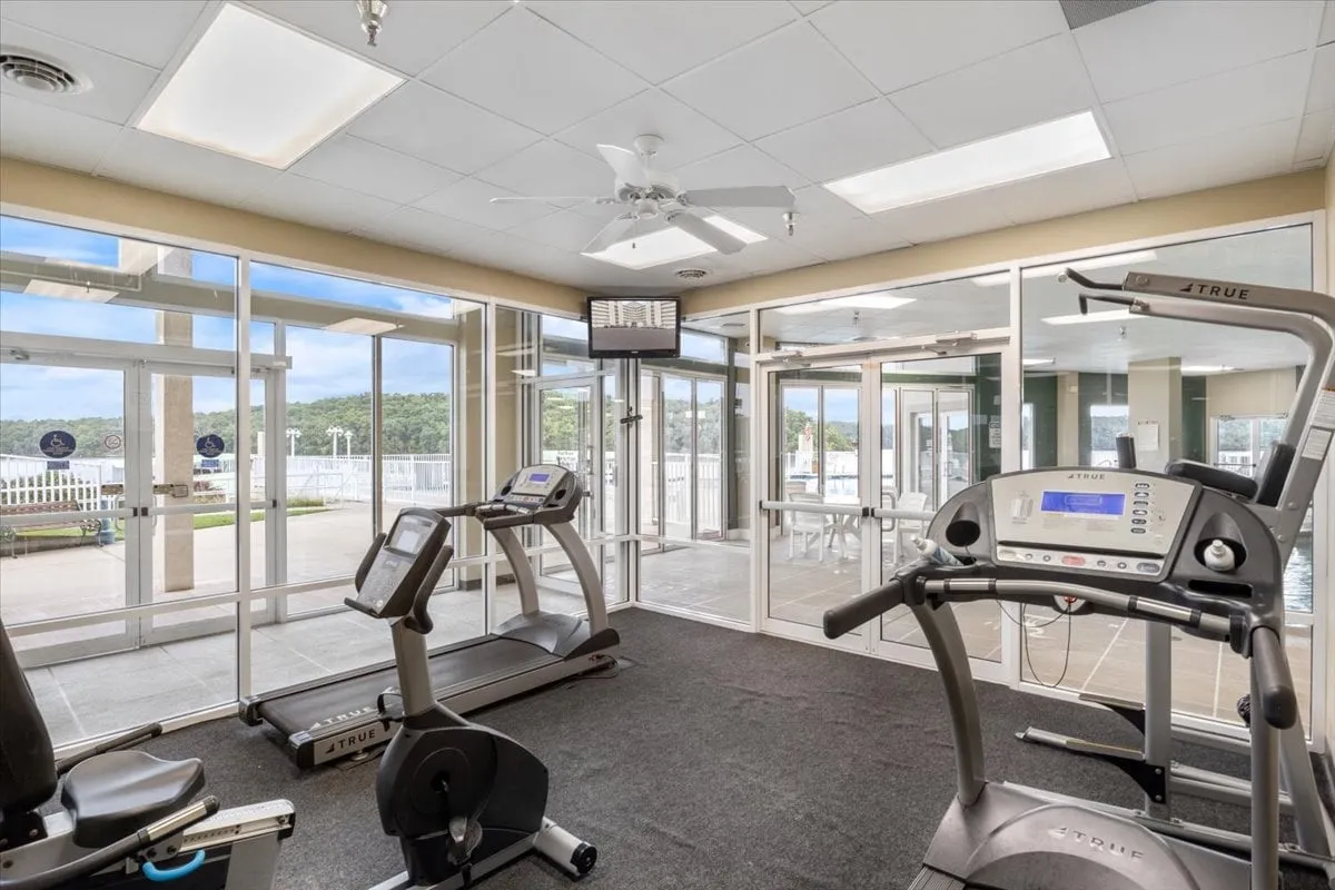 A well-equipped gym space features treadmills, an elliptical machine, large windows that let in natural light, and a television. The modern layout and motivational ambiance make it an inviting spot for energizing workouts and personal fitness routines.