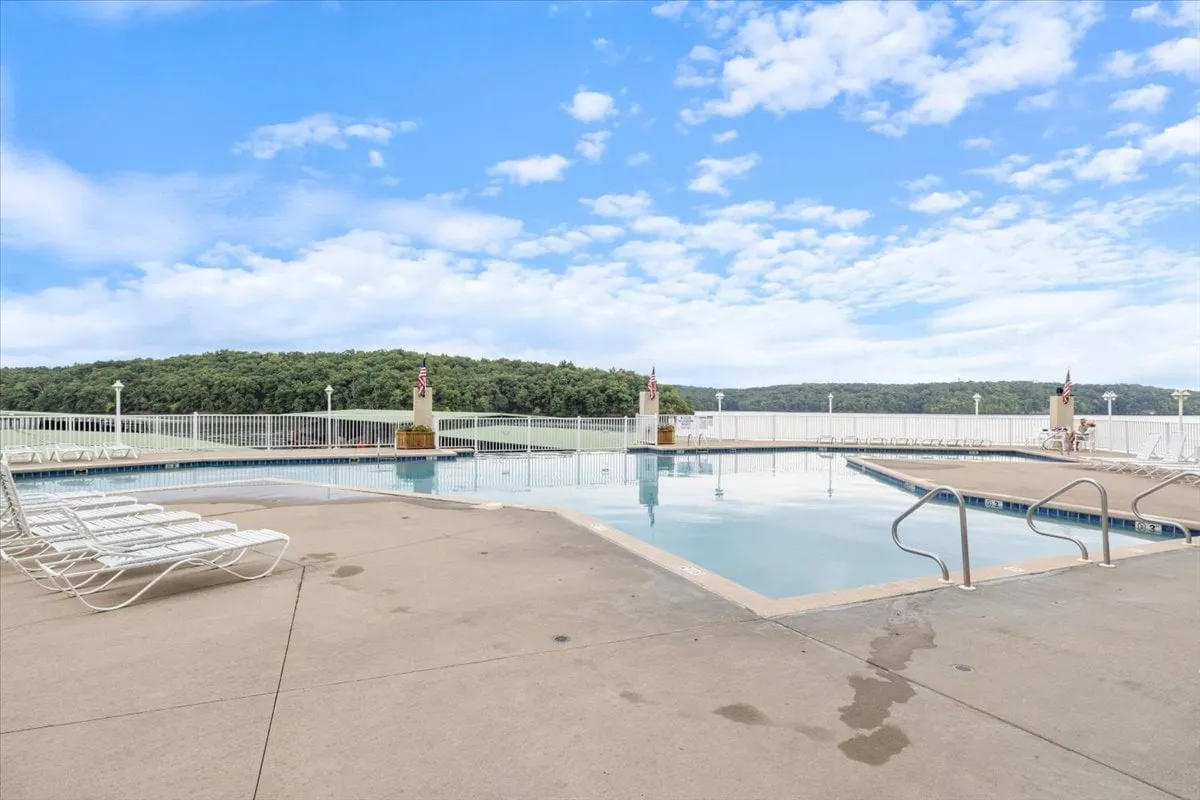 An inviting exterior swimming pool is surrounded by lush landscaping and comfortable lounge chairs. The tranquil water and open-air setting evoke a sense of vacation and leisure, perfect for sunbathing, swimming, or gathering with friends by the pool.