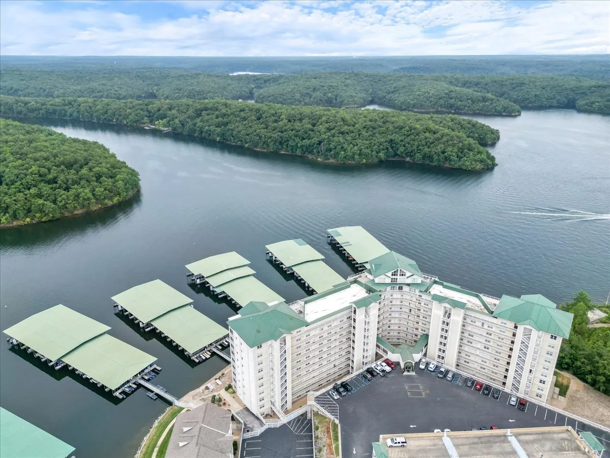 This image showcases a large waterfront building set beside marinas filled with boats and surrounded by forested hills. The expansive lake is visible, inviting thoughts of outdoor activities and relaxation by the water.