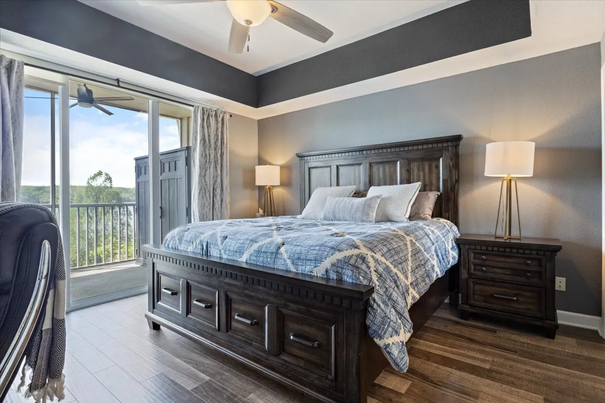 A spacious bedroom featuring a plush king-size bed framed by two nightstands with softly glowing lamps. Large windows bathe the room in natural light and offer a serene view, while the layout is uncluttered, inviting relaxation and comfort.